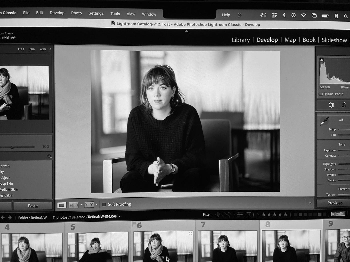 A computer monitor displays the Adobe Lightroom Classic interface, showing a black-and-white portrait of a woman seated in a chair with a filmstrip of similar shots along the bottom.