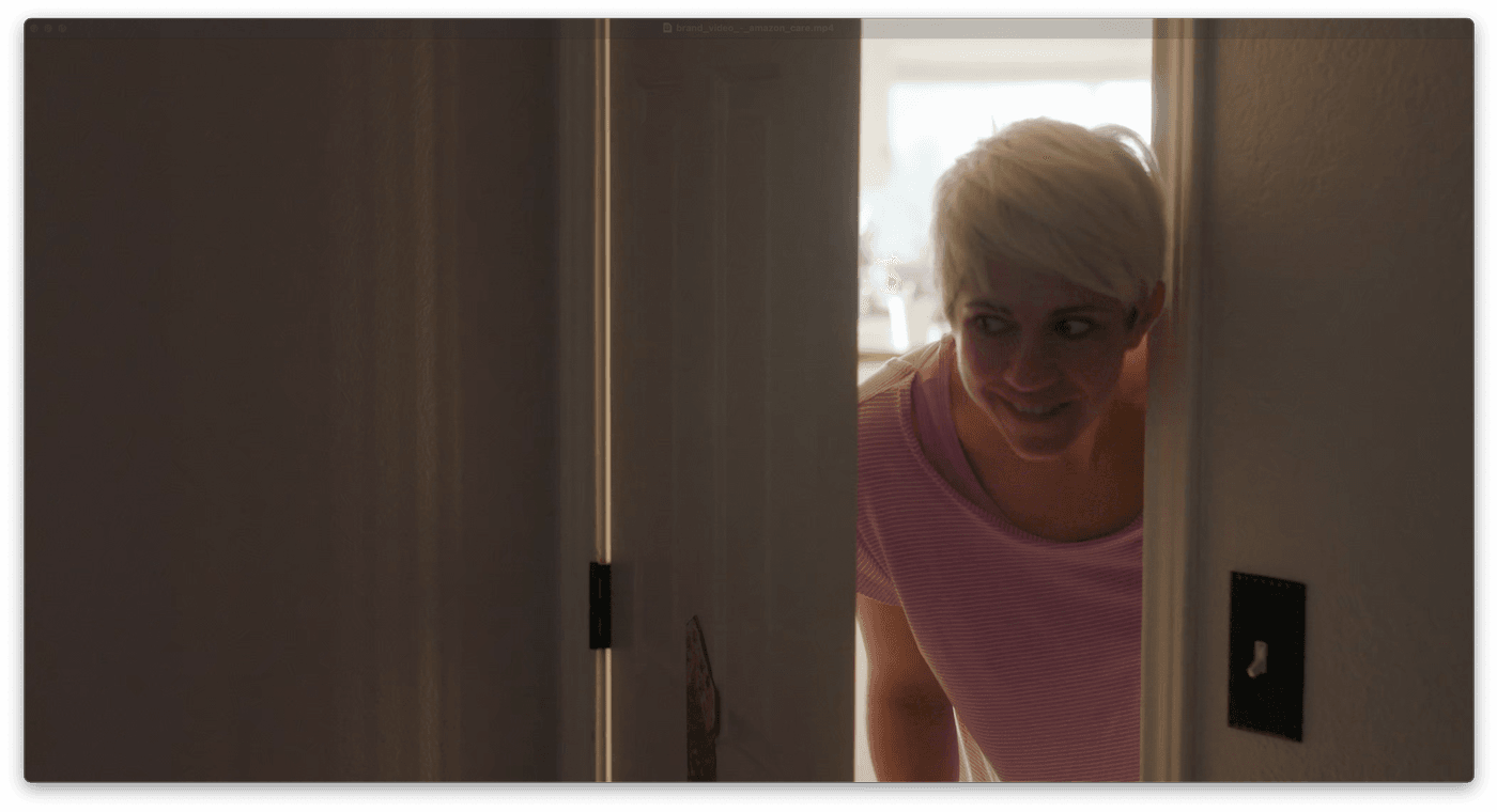 A woman with short blonde hair smiles while peeking through a partially open door.