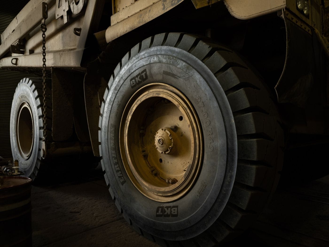 Close-up side view of a large, yellow mining dump truck showing its massive BKT Earthmax tire and wheel assembly in a dimly lit industrial setting.
