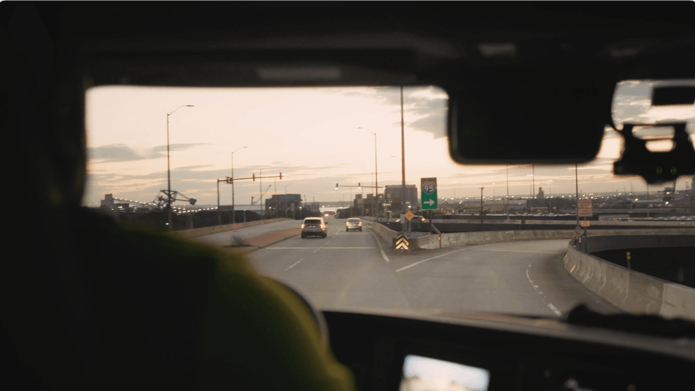 The view from inside the cab of a vehicle shows a road splitting at a highway interchange sign pointing toward Interstate 95 during sunset.
