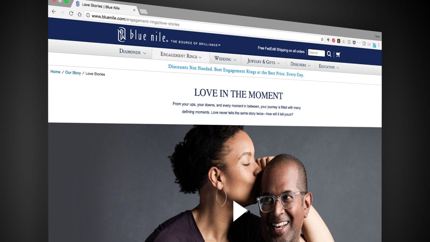 A screen capture shows the Blue Nile website’s "Love Stories" page, featuring the heading "LOVE IN THE MOMENT" above a promotional video image of a woman kissing a man on the head.