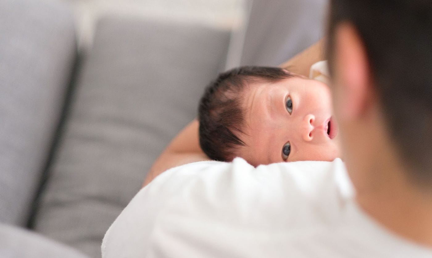 An adult holds a newborn baby in their arms, who is looking intently towards the person holding them.