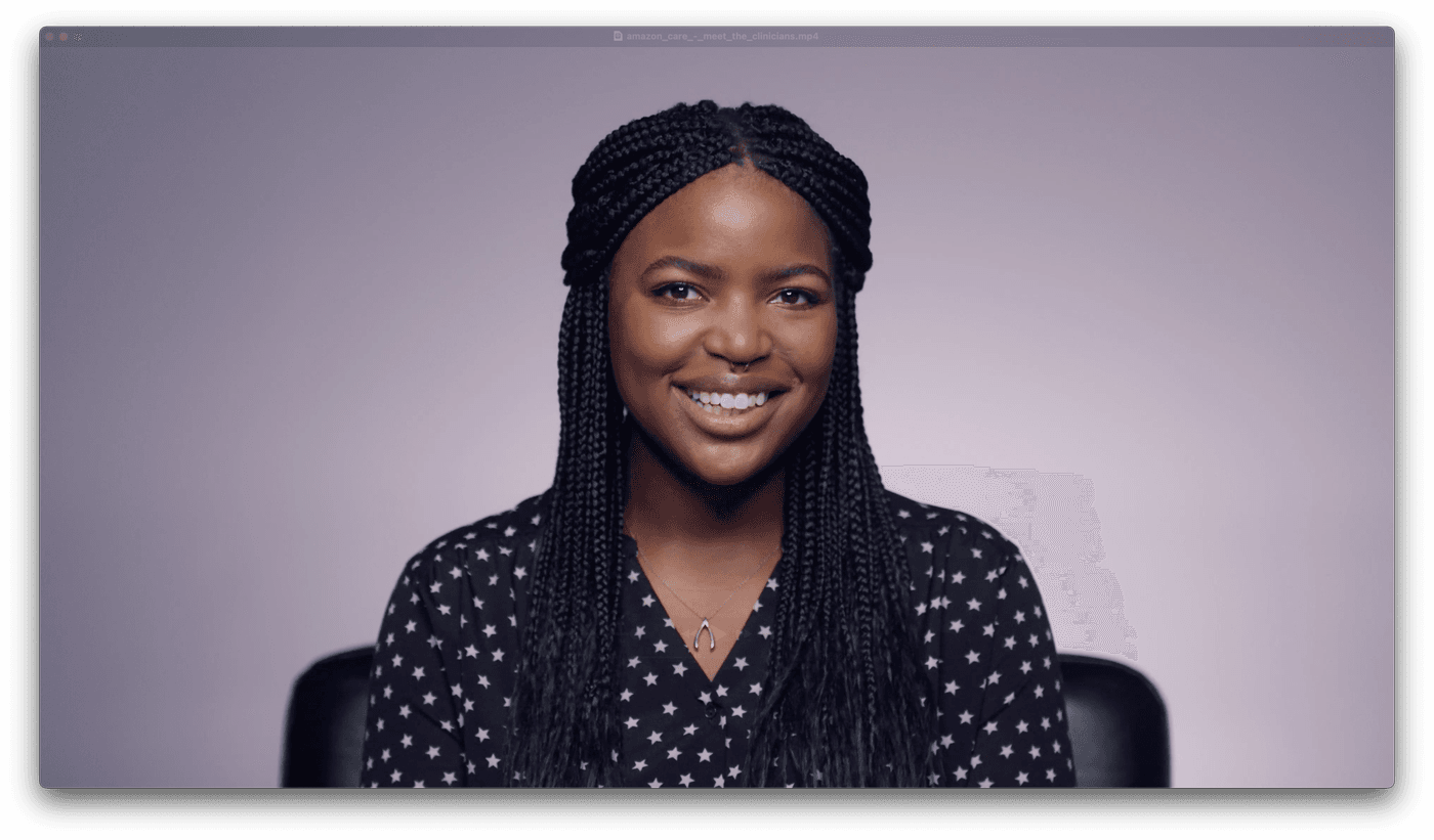 A smiling young woman with braided hair and a septum piercing wears a star-patterned shirt and a gold wishbone necklace against a soft, light-purple background.