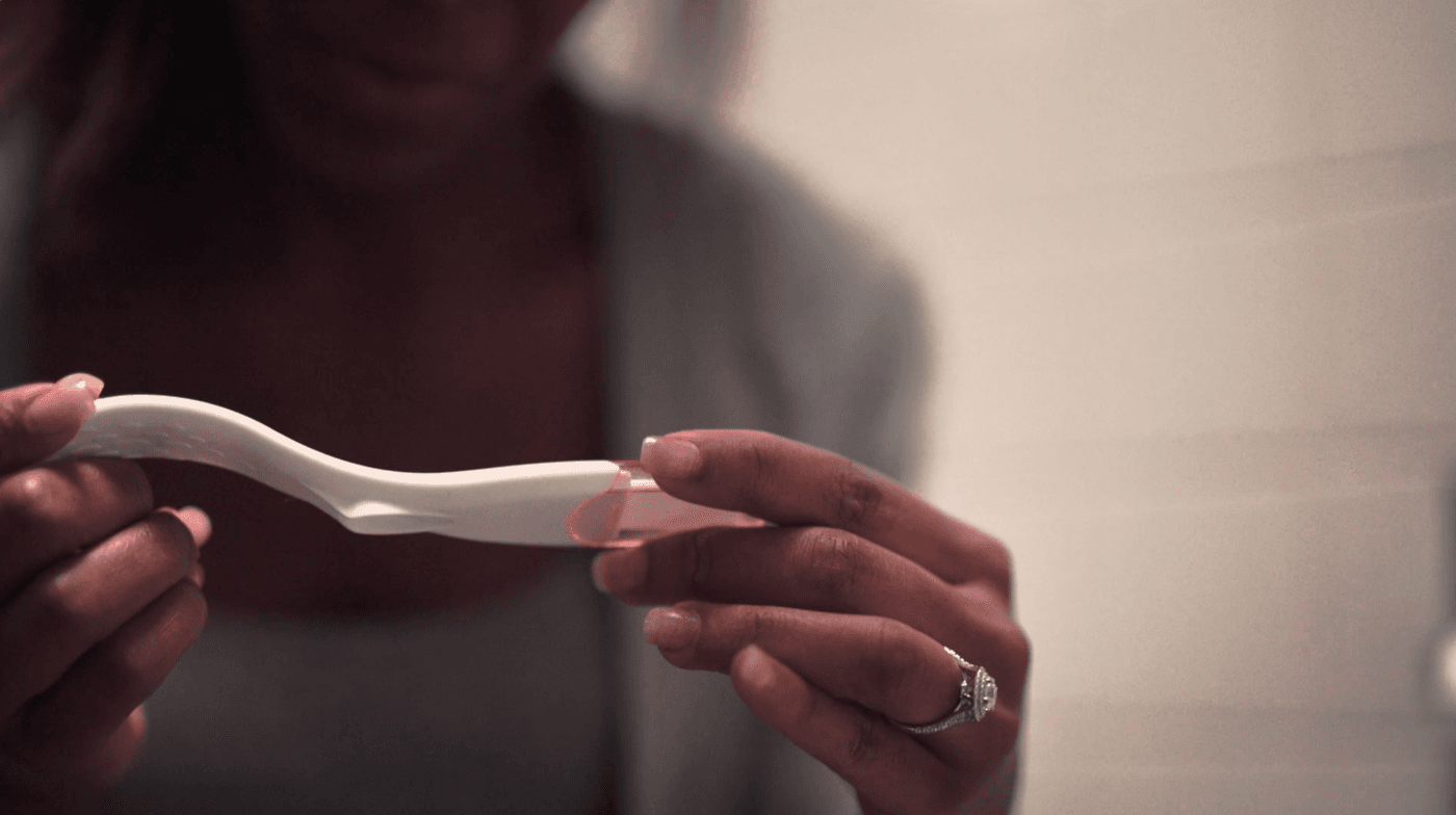 A woman with a diamond ring on her finger holds a pregnancy test in her hands.
