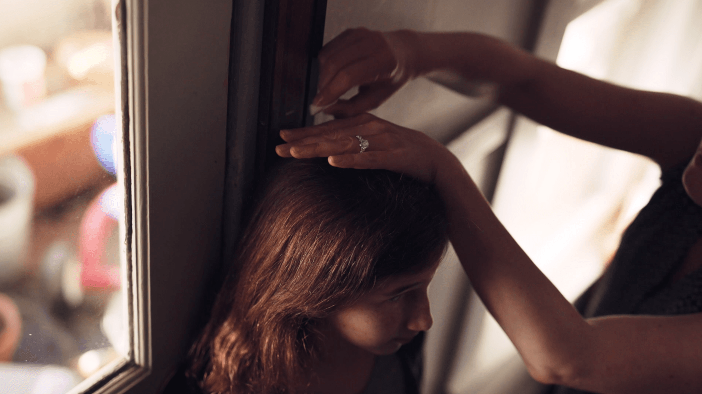 A person's hand with a ring rests on top of a young girl's head as they measure her height against a door frame.