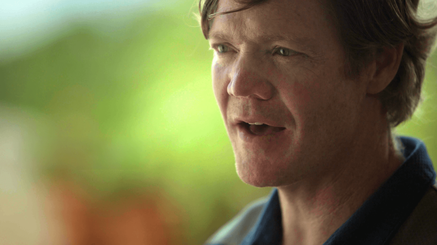 A medium close-up shot of a fair-skinned man with brown hair and light eyes looking slightly off-camera with his mouth slightly open.