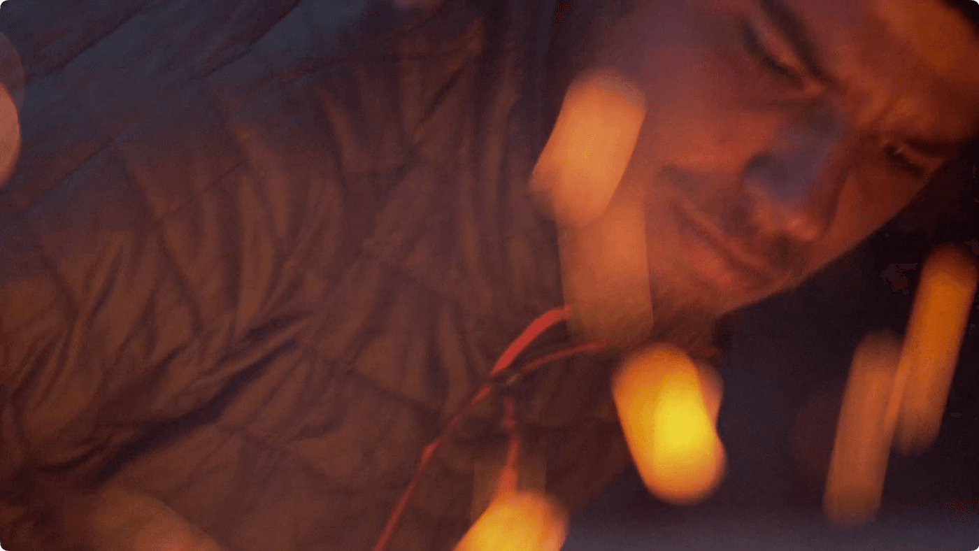 A man in a dark quilted jacket is partially obscured by blurred, glowing orange light streaks in a dimly lit, cozy setting.